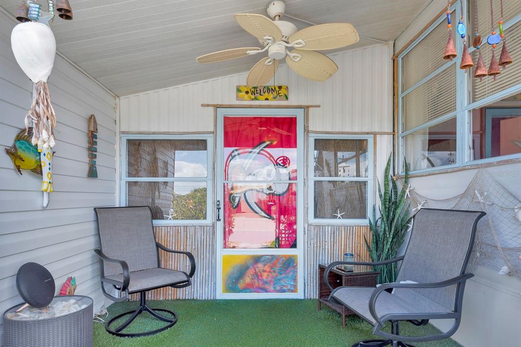 A covered porch features green turf flooring, two chairs, a ceiling fan, and coastal decor — 515 50TH AVENUE TERRACE W, BRADENTON, FL