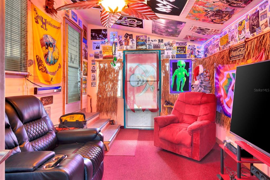A room with red carpet, a black leather sofa, a red recliner, and walls covered in posters — 515 50TH AVENUE TERRACE W, BRADENTON, FL
