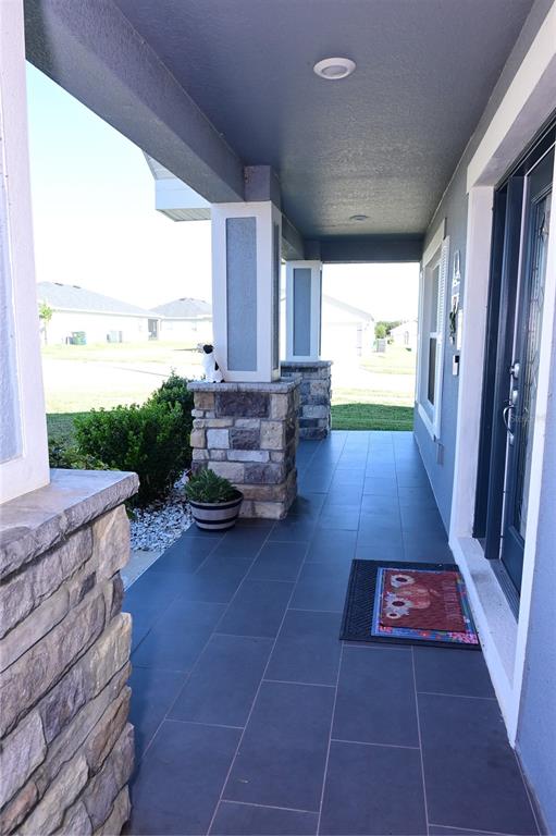 A covered front porch features dark tile flooring, stone-based columns, and a glass-paneled front door — 891 GALLOWAY STREET, LAKE ALFRED, FL