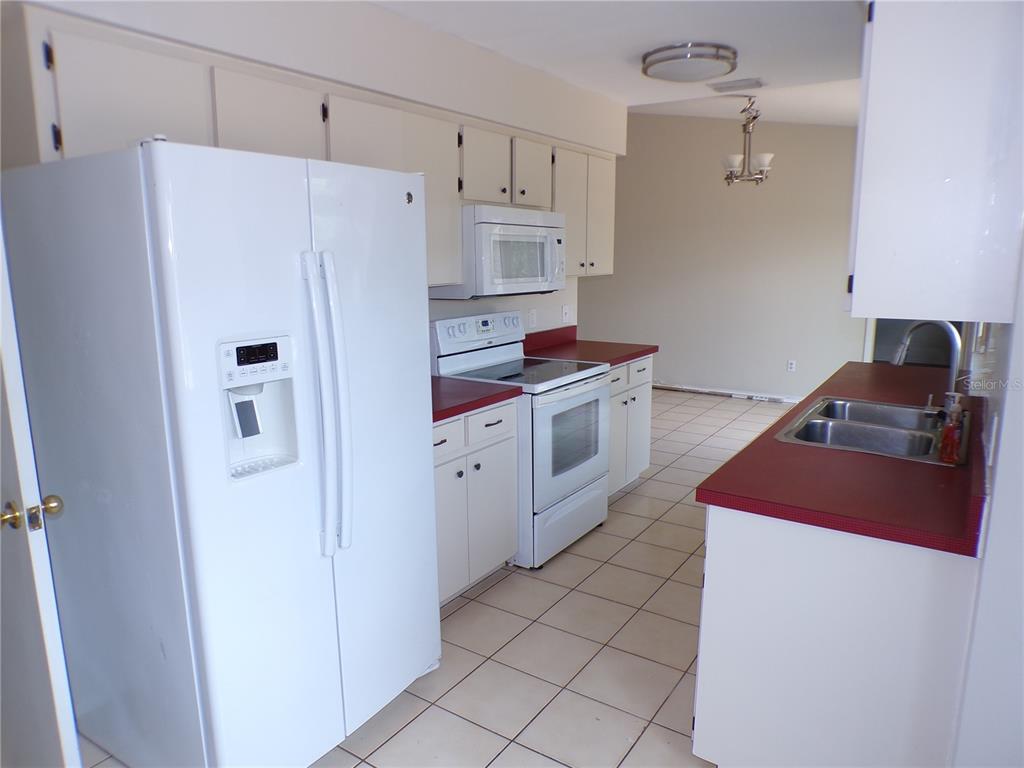 A kitchen features white cabinets, red countertops, a double sink, and light-colored floor tiles — 10104 WILLMINGTON BOULEVARD, ENGLEWOOD, FL