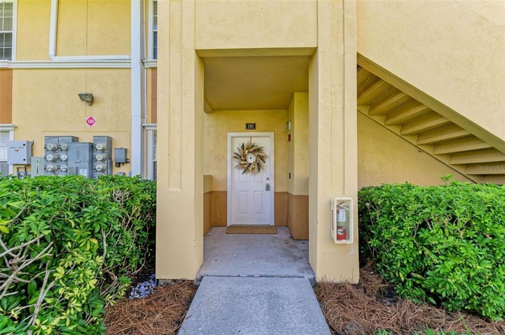 A ground-level apartment entrance with a white door, a wreath, and an adjacent outdoor staircase — 1195 VILLAGIO CIRCLE UNIT 101, SARASOTA, FL