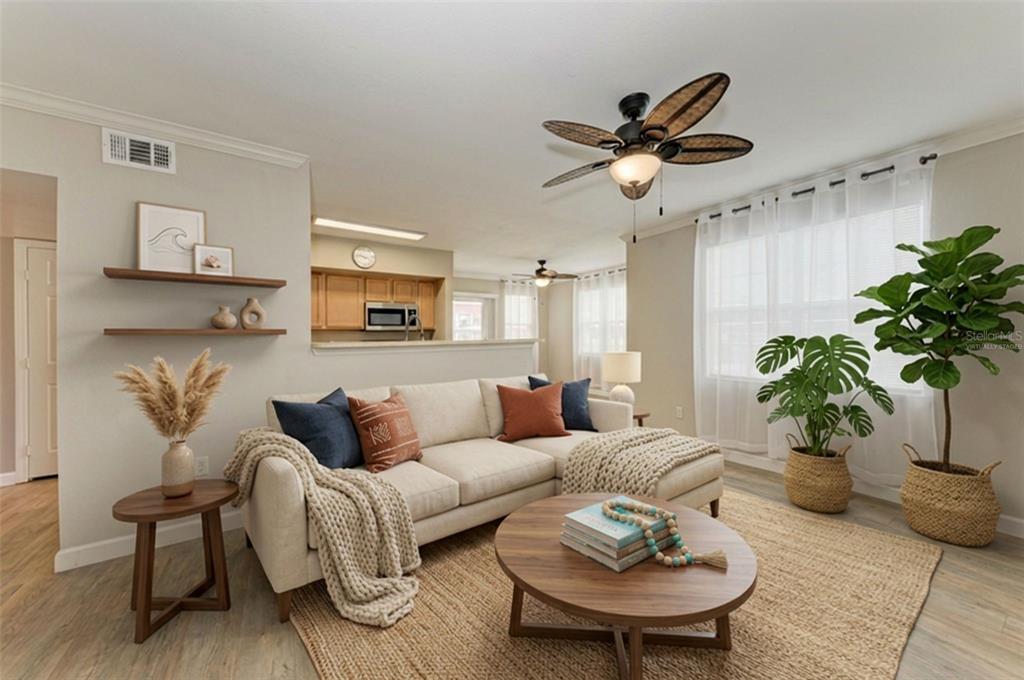A living room with a beige sectional, round wooden coffee table, and two large potted plants — 1195 VILLAGIO CIRCLE UNIT 101, SARASOTA, FL