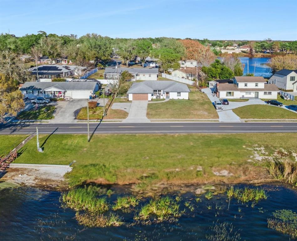 An aerial view shows three houses across a road from a lakefront grassy lot — 1106 LAKE ARIANA BOULEVARD, AUBURNDALE, FL