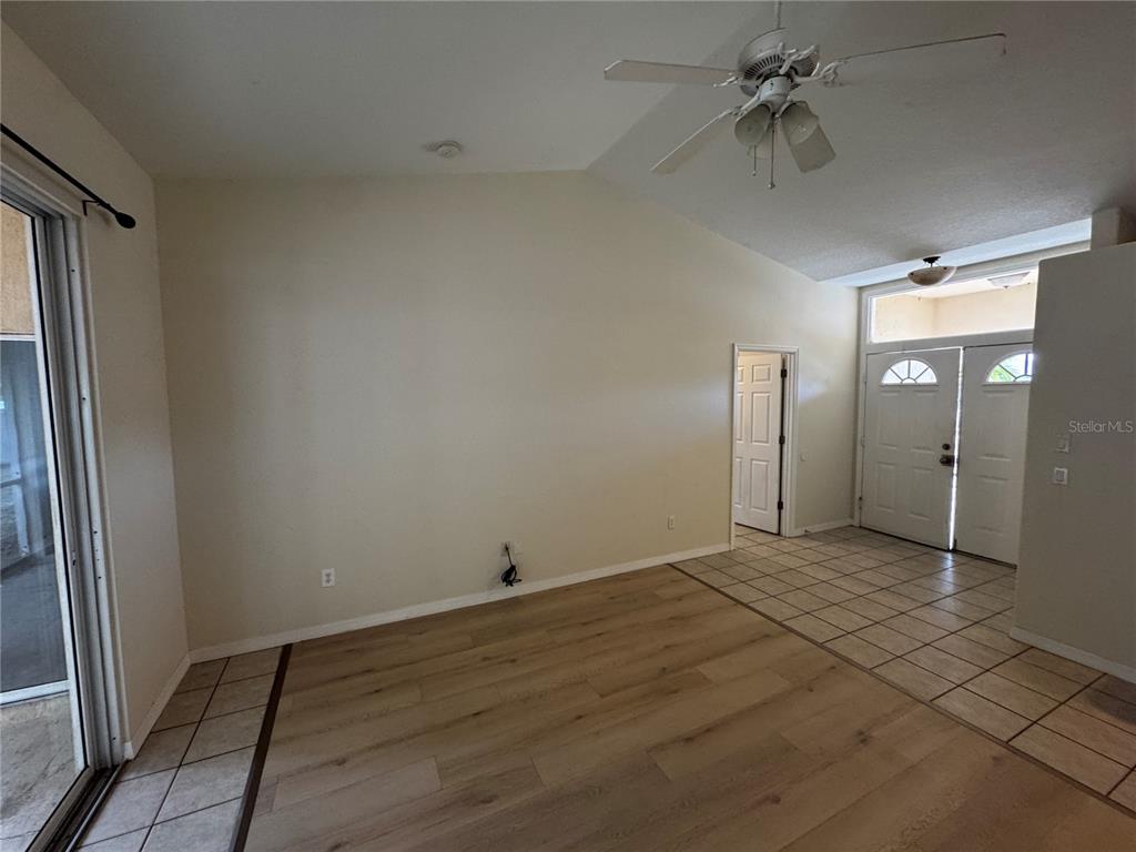 A living room features vaulted ceilings, a ceiling fan, wood-look flooring, and tiled entryways — 8234 MOSSBORGER AVENUE, NORTH PORT, FL