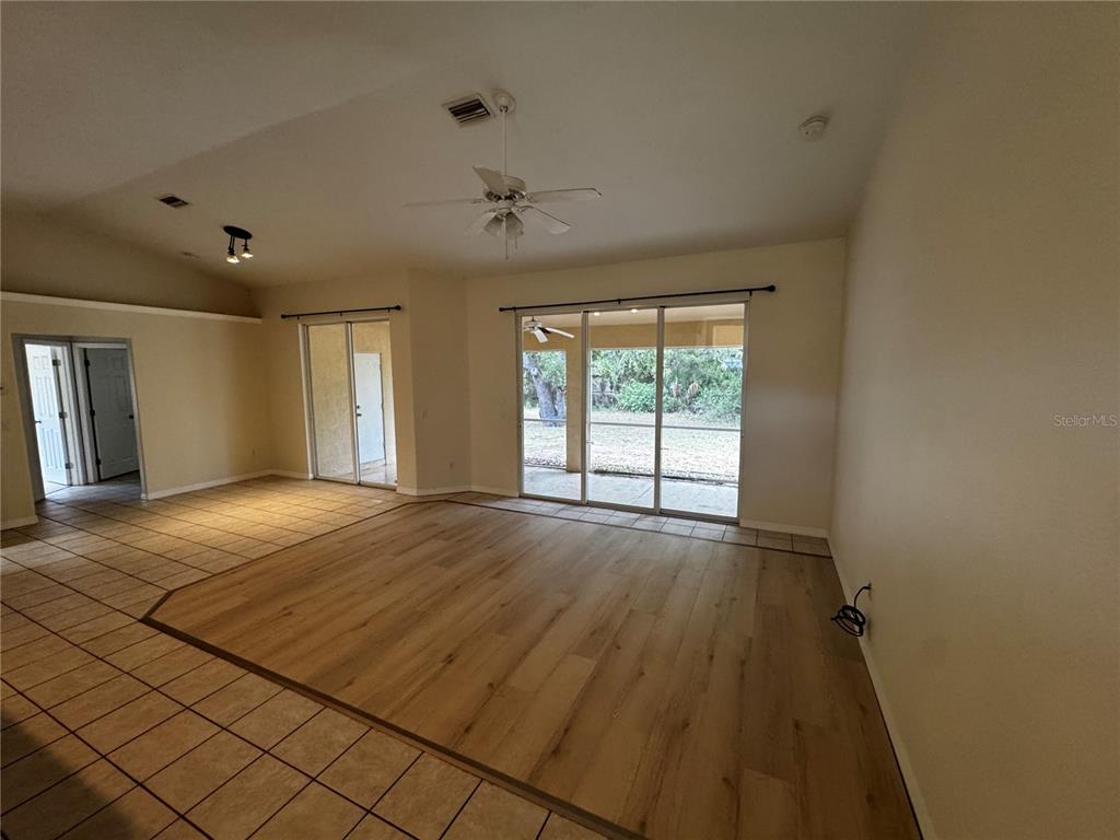 An open living area features light wood-look flooring, tile borders, and sliding glass patio doors — 8234 MOSSBORGER AVENUE, NORTH PORT, FL
