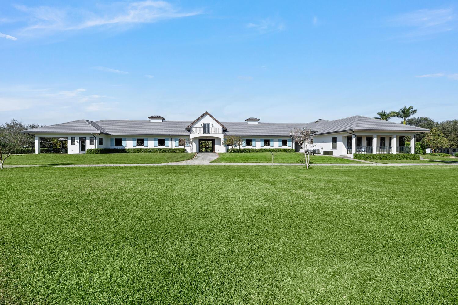 A wide, single-story white house with a gray tile roof sits behind a large lawn — 4915 Stables Way, Wellington FL 33414, WELLINGTON, FL