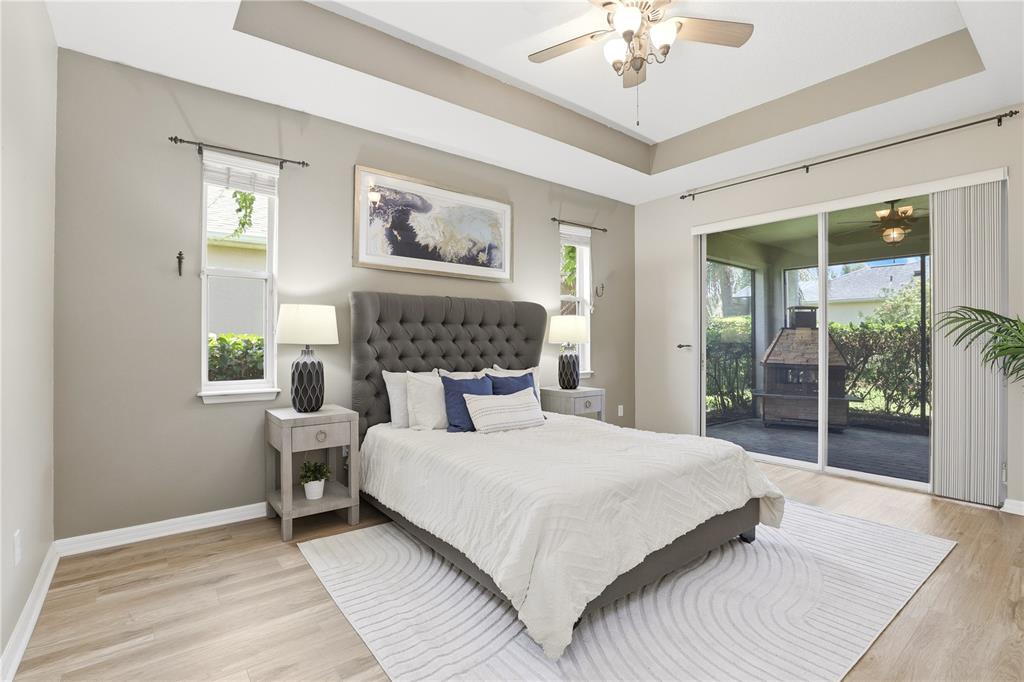 A bedroom features a tufted headboard, light wood flooring, a tray ceiling, and sliding glass doors — 3904 HEIRLOOM ROSE PLACE, OVIEDO, FL