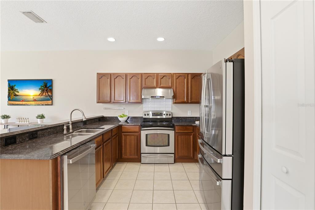 A kitchen features wood cabinets, granite countertops, stainless steel appliances, and tile flooring — 3904 HEIRLOOM ROSE PLACE, OVIEDO, FL