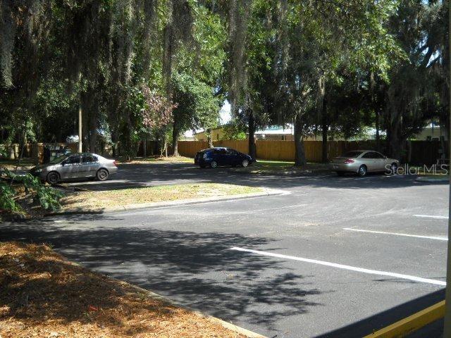 A paved parking lot with several cars parked under large trees near a wooden fence — 37037 STATE ROAD 54, ZEPHYRHILLS, FL