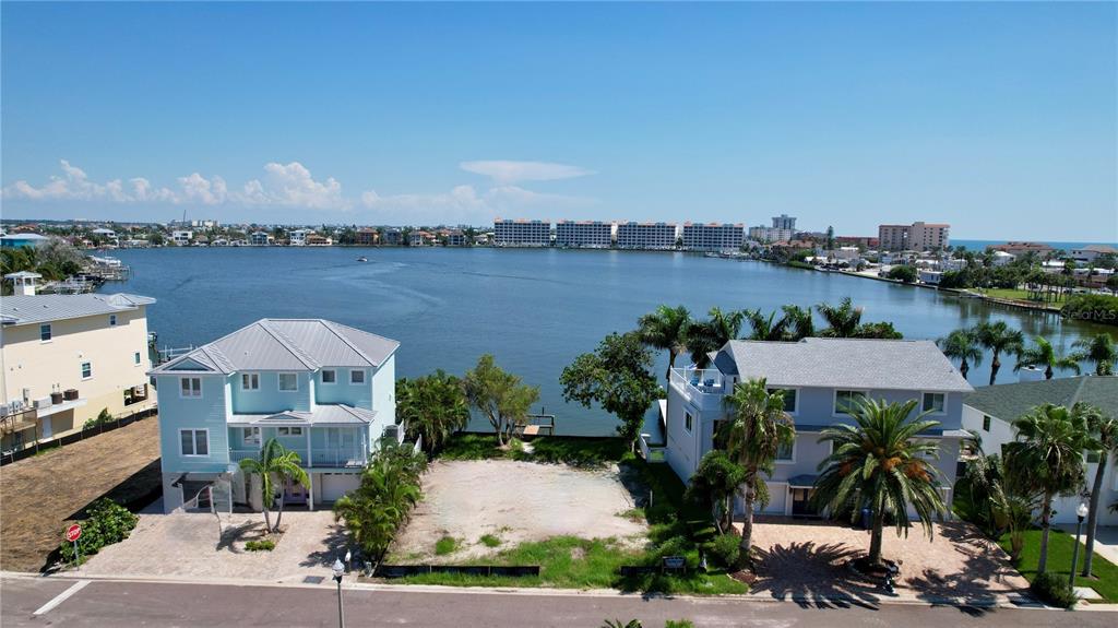 An aerial view shows a vacant waterfront lot situated between two multi-story houses — 415 180TH AVENUE E, REDINGTON SHORES, FL