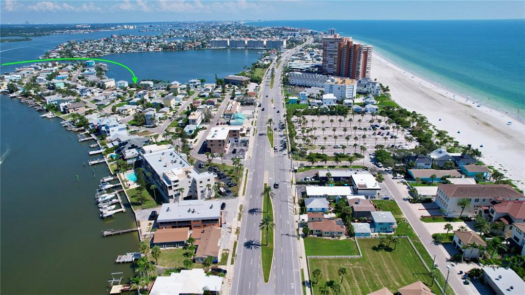 An aerial view shows a coastal neighborhood with houses, a road, and a beach — 415 180TH AVENUE E, REDINGTON SHORES, FL