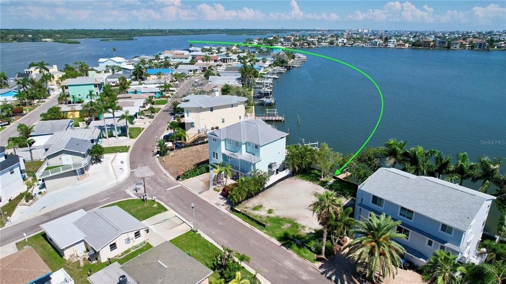 An aerial view shows a vacant waterfront lot situated between two multi-story houses — 415 180TH AVENUE E, REDINGTON SHORES, FL