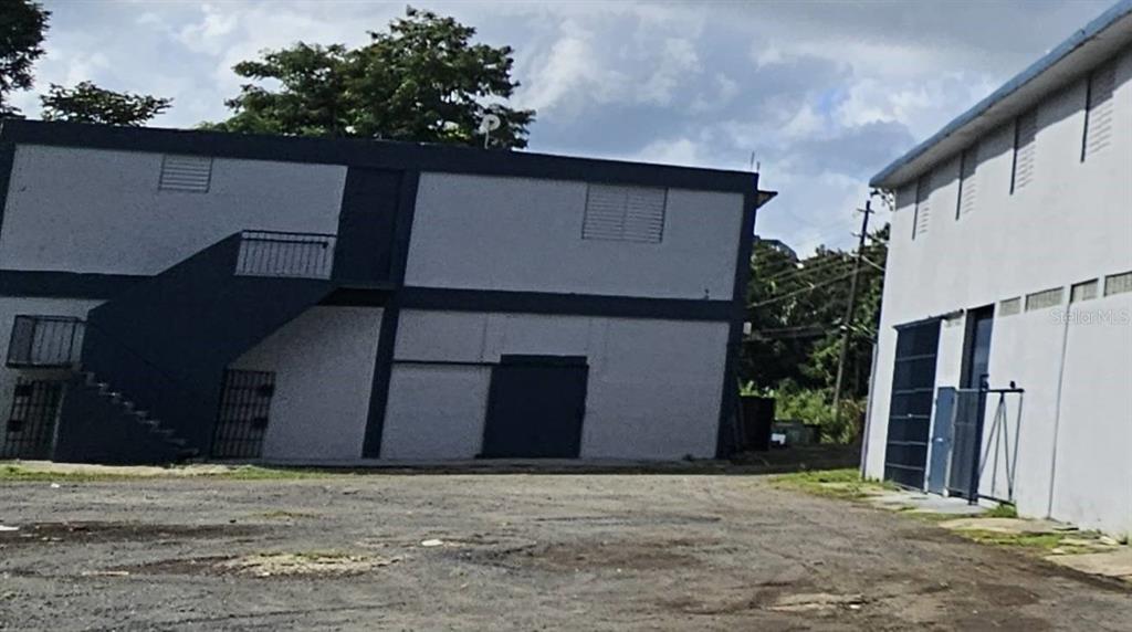An exterior view of two adjacent commercial buildings with a gravel lot in the foreground — 1 MUÑOZ RIVERA, SAN JUAN, PR