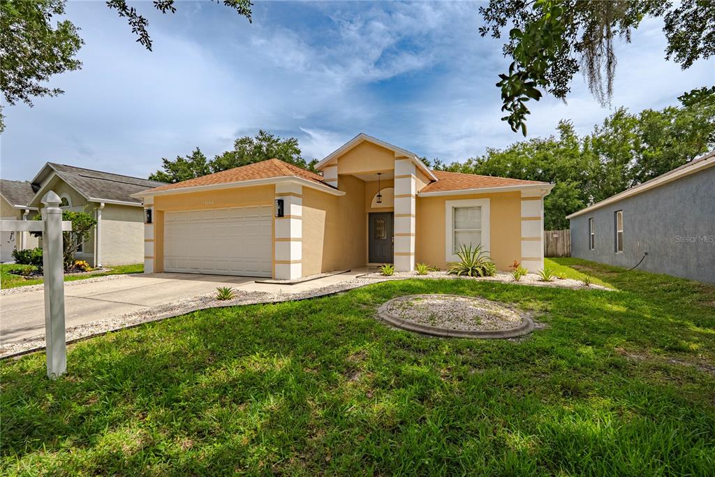 A single-story house with a tan stucco exterior, white trim, and a two-car garage — 19204 WOOD SAGE DRIVE, TAMPA, FL