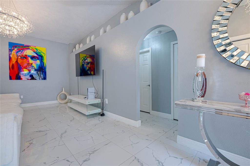 A living room features light gray walls, white marble-look tile flooring, and an arched doorway — 19204 WOOD SAGE DRIVE, TAMPA, FL