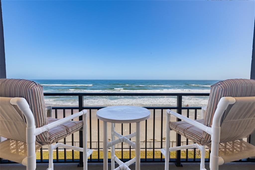 A balcony with two chairs and a small table overlooks the ocean and beach — 2301 S ATLANTIC AVENUE UNIT 403, DAYTONA BEACH, FL