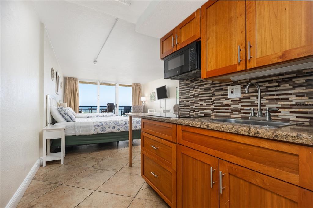 A studio apartment features a kitchenette with wood cabinets, stone countertops, and a bedroom area — 2301 S ATLANTIC AVENUE UNIT 403, DAYTONA BEACH, FL