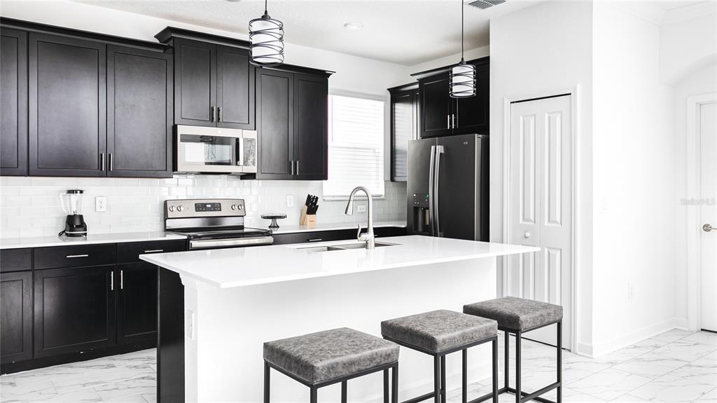 A kitchen features black cabinets, white countertops, a central island with stools, and stainless appliances — 989 LEADER STREET, DAVENPORT, FL