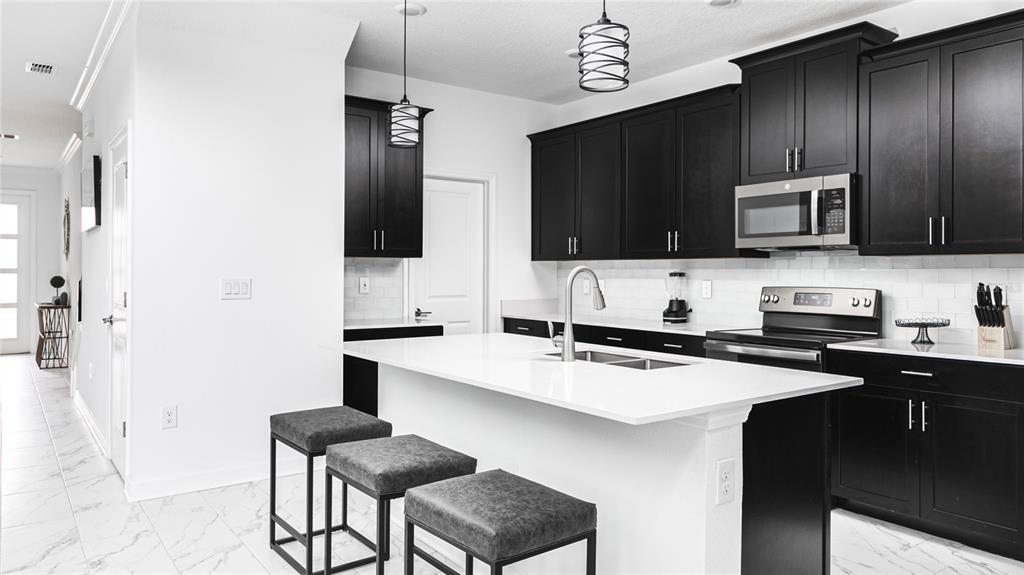 A modern kitchen features black cabinets, white countertops, a central island, and white tile flooring — 989 LEADER STREET, DAVENPORT, FL