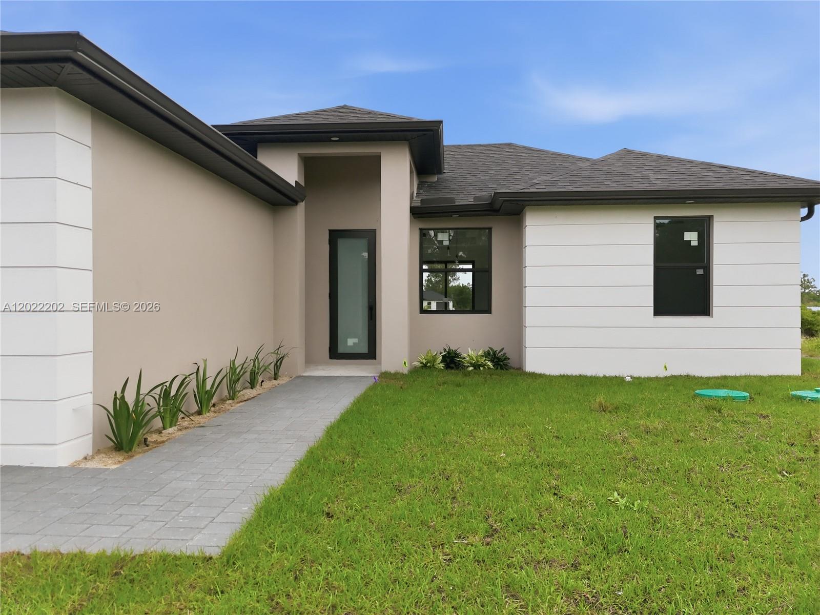 The exterior of a modern single-story house features a paved walkway and a front entrance — 1222 Earnest St E, Lehigh Acres FL 33974, LEHIGH ACRES, FL
