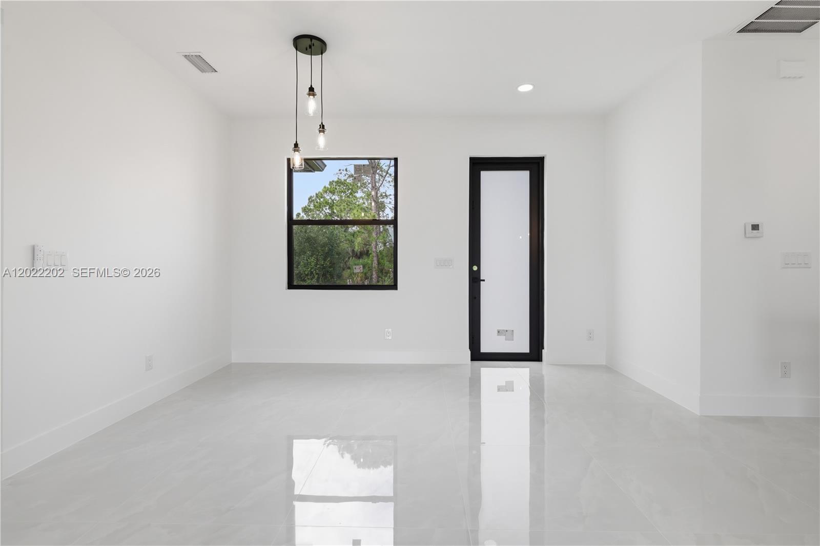A minimalist room features white walls, glossy tile flooring, a pendant light, and a glass door — 1222 Earnest St E, Lehigh Acres FL 33974, LEHIGH ACRES, FL