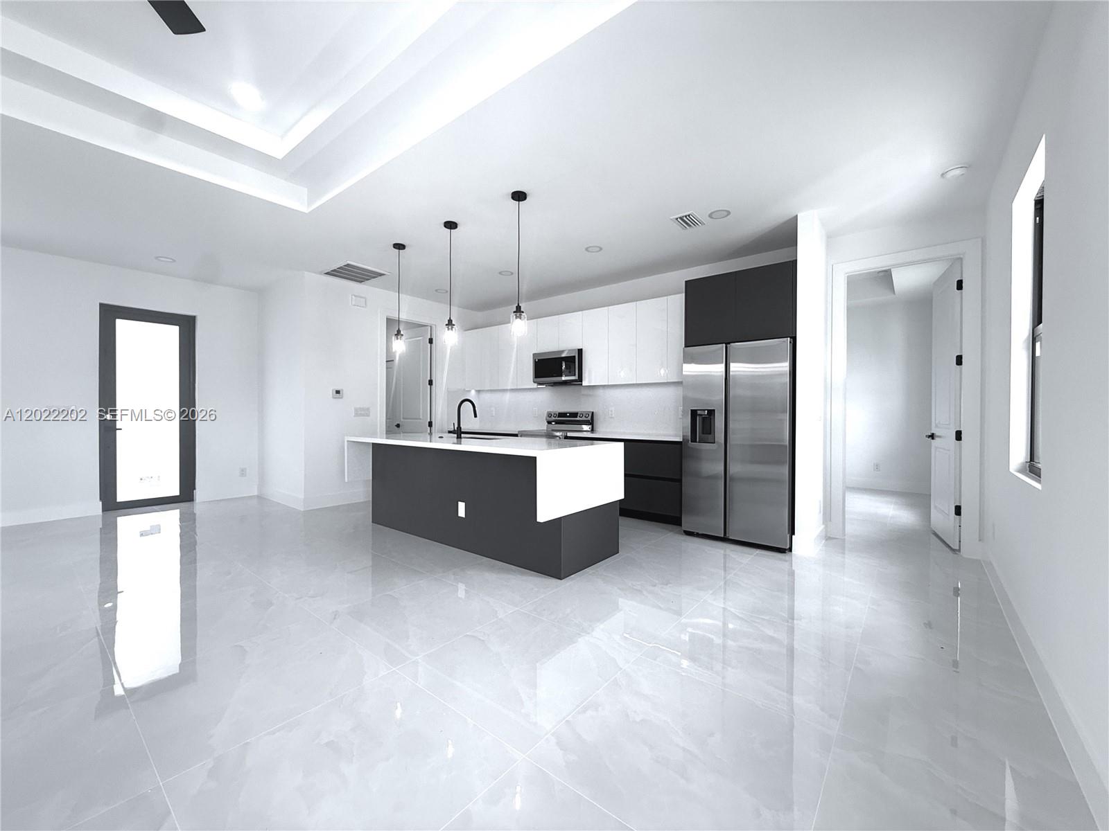 A modern kitchen features a two-tone island, white upper cabinets, and polished tile flooring — 1222 Earnest St E, Lehigh Acres FL 33974, LEHIGH ACRES, FL