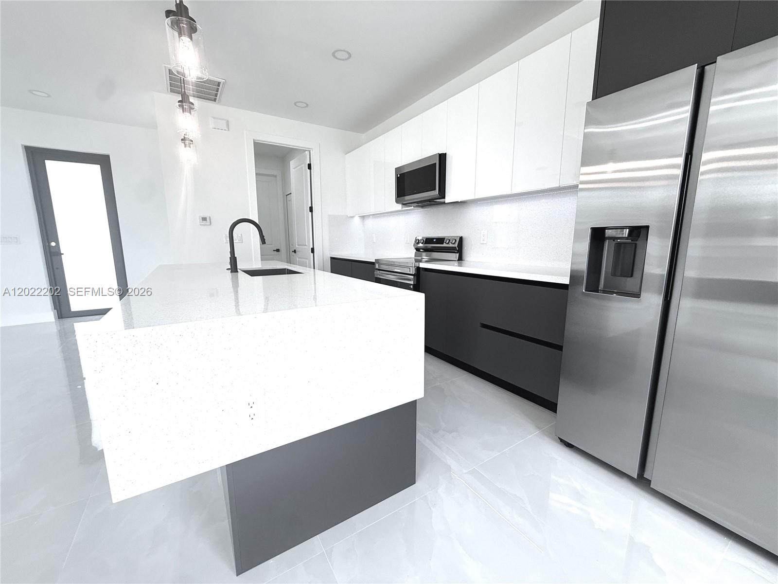 A modern kitchen features a white quartz island, dark lower cabinets, and white upper cabinets — 1222 Earnest St E, Lehigh Acres FL 33974, LEHIGH ACRES, FL