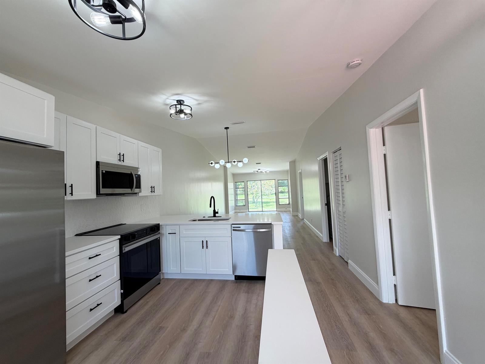 A modern kitchen features white cabinets, stainless steel appliances, and light wood-look flooring — 18720 Schooner Drive, Boca Raton FL 33496, BOCA RATON, FL