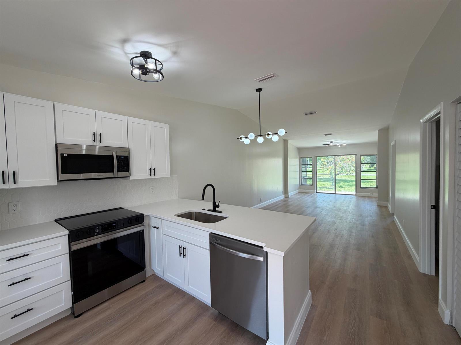 A kitchen with white cabinets, stainless steel appliances, and quartz countertops opens to a living area — 18720 Schooner Drive, Boca Raton FL 33496, BOCA RATON, FL