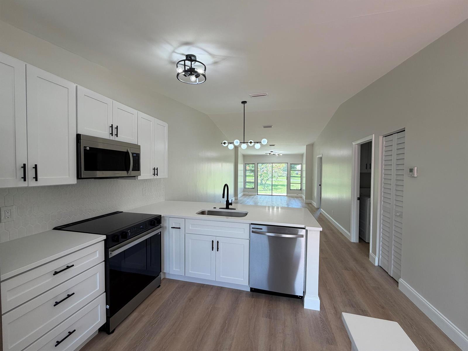 A modern kitchen with white cabinets, stainless steel appliances, and wood-look flooring — 18720 Schooner Drive, Boca Raton FL 33496, BOCA RATON, FL