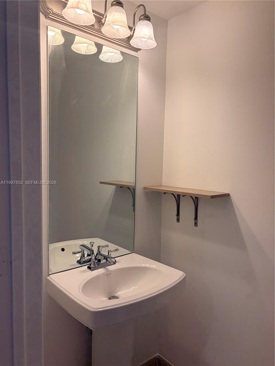 A bathroom features a pedestal sink, a wall-mounted shelf, and a three-light vanity fixture — 55 Merrick Way # 534, Coral Gables FL 33134, CORAL GABLES, FL