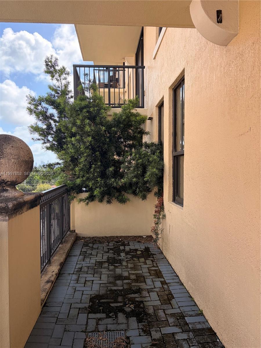 A balcony with dark brick pavers, a metal railing, and a large overgrown evergreen shrub — 55 Merrick Way # 534, Coral Gables FL 33134, CORAL GABLES, FL
