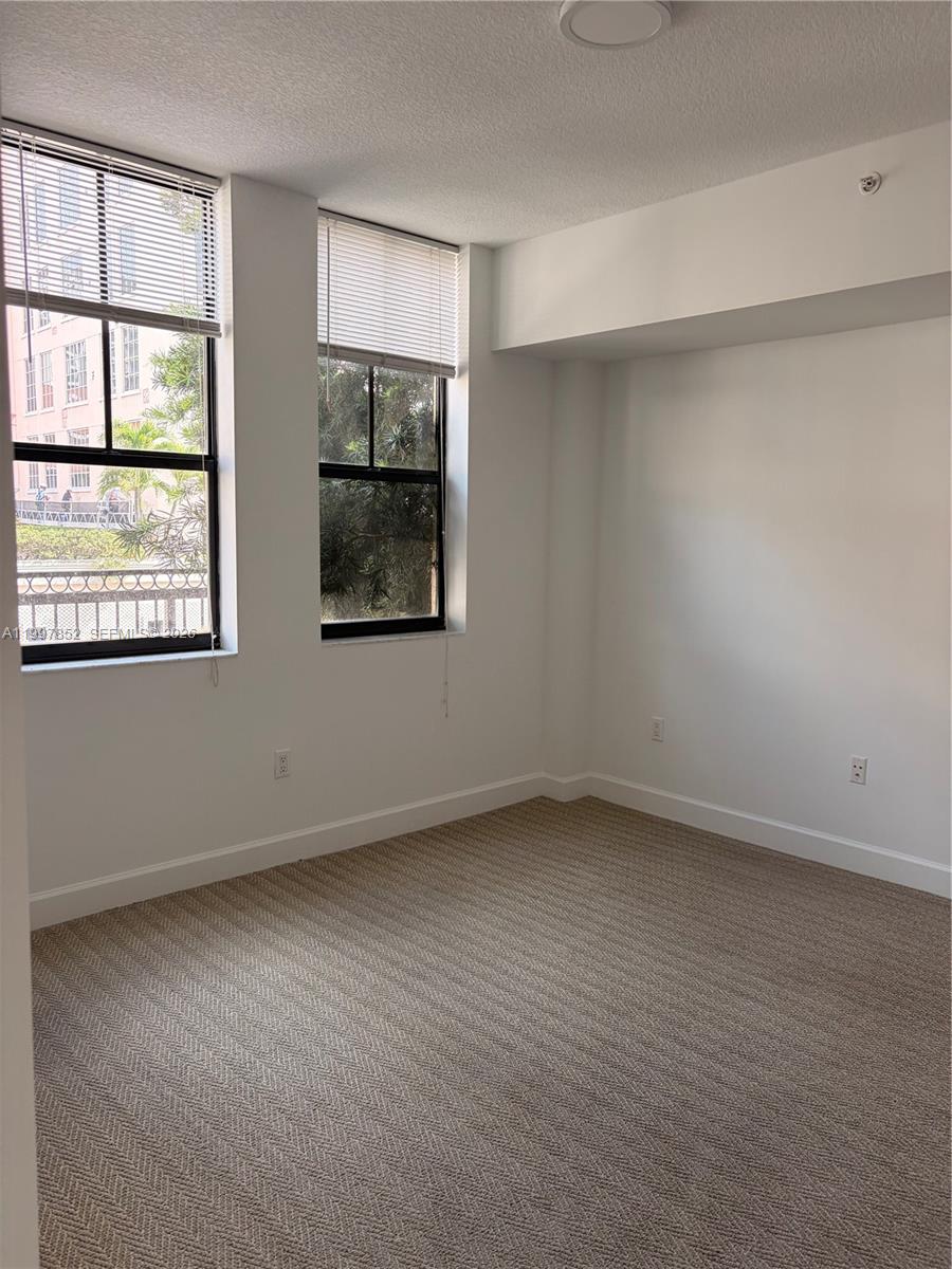An empty bedroom features beige carpet, white walls, and two windows with white blinds — 55 Merrick Way # 534, Coral Gables FL 33134, CORAL GABLES, FL