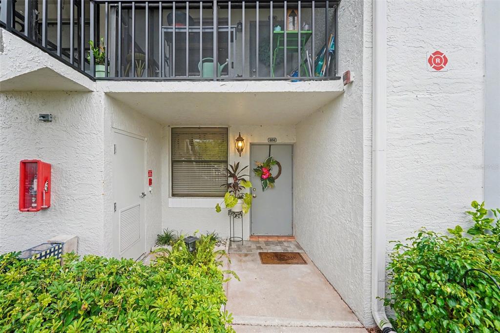 The exterior view shows a ground-floor apartment entrance with a balcony above and landscaping — 1945 PELICAN LANDING BOULEVARD UNIT 614, CLEARWATER, FL