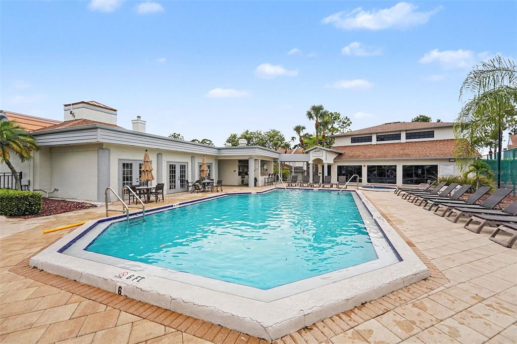 An outdoor swimming pool with lounge chairs and a clubhouse building in the background — 1945 PELICAN LANDING BOULEVARD UNIT 614, CLEARWATER, FL