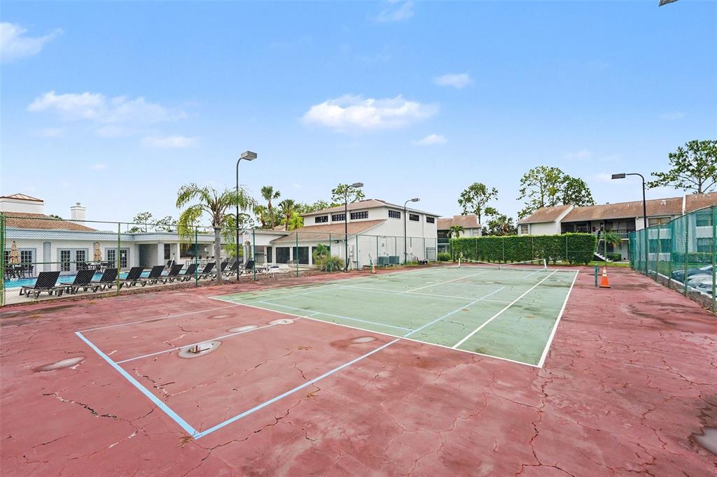 A tennis court with a red and green surface sits outdoors near a swimming pool — 1945 PELICAN LANDING BOULEVARD UNIT 614, CLEARWATER, FL