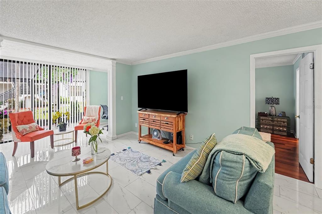 A living room features light blue walls, white tile flooring, a television, and a sofa — 1945 PELICAN LANDING BOULEVARD UNIT 614, CLEARWATER, FL