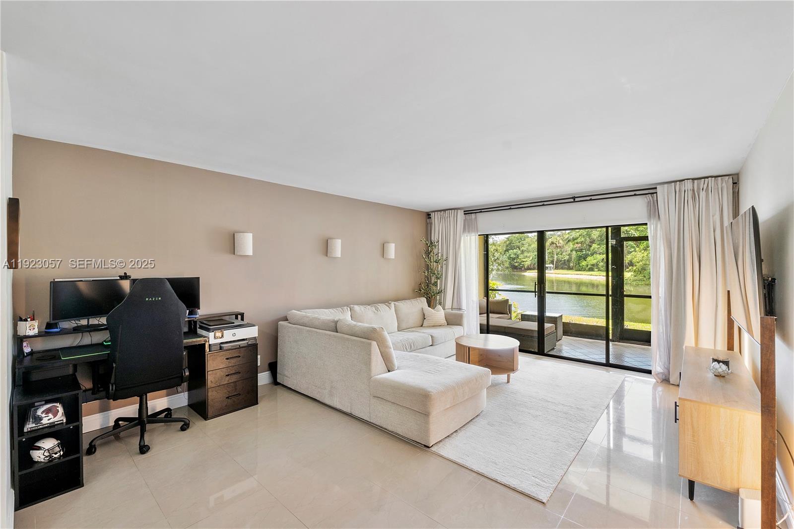 A living room features a sectional sofa, a desk setup, and sliding doors overlooking water — 1706 Hammock Blvd # 1706, Coconut Creek FL 33063, COCONUT CREEK, FL