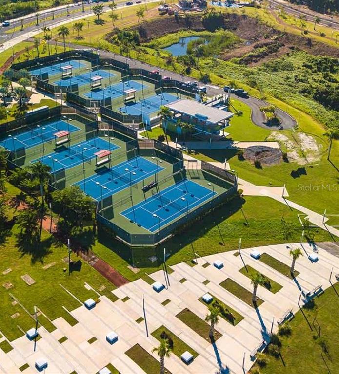 An aerial view shows multiple blue tennis courts surrounded by green landscaping and paved walkways — Calle Central Park URB. RIVIERA VILLAGE, BAYAMON, PR