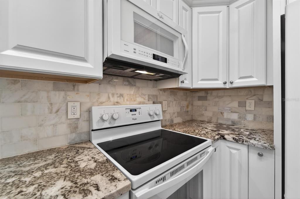 A kitchen with white cabinets, a glass-top stove, a microwave, and marble tile backsplash — 658 GREEN VALLEY ROAD UNIT B3, PALM HARBOR, FL