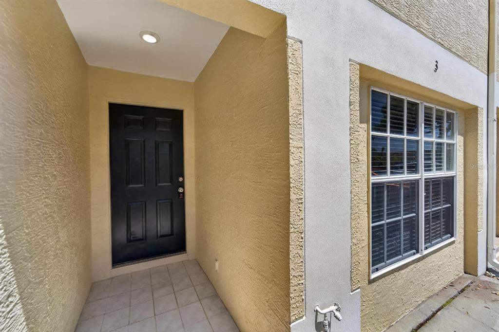 A black front door sits in a recessed entryway next to a window with shutters — 658 GREEN VALLEY ROAD UNIT B3, PALM HARBOR, FL