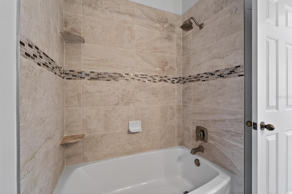A tiled bathtub and shower combination features a decorative mosaic accent strip and bronze fixtures — 658 GREEN VALLEY ROAD UNIT B3, PALM HARBOR, FL