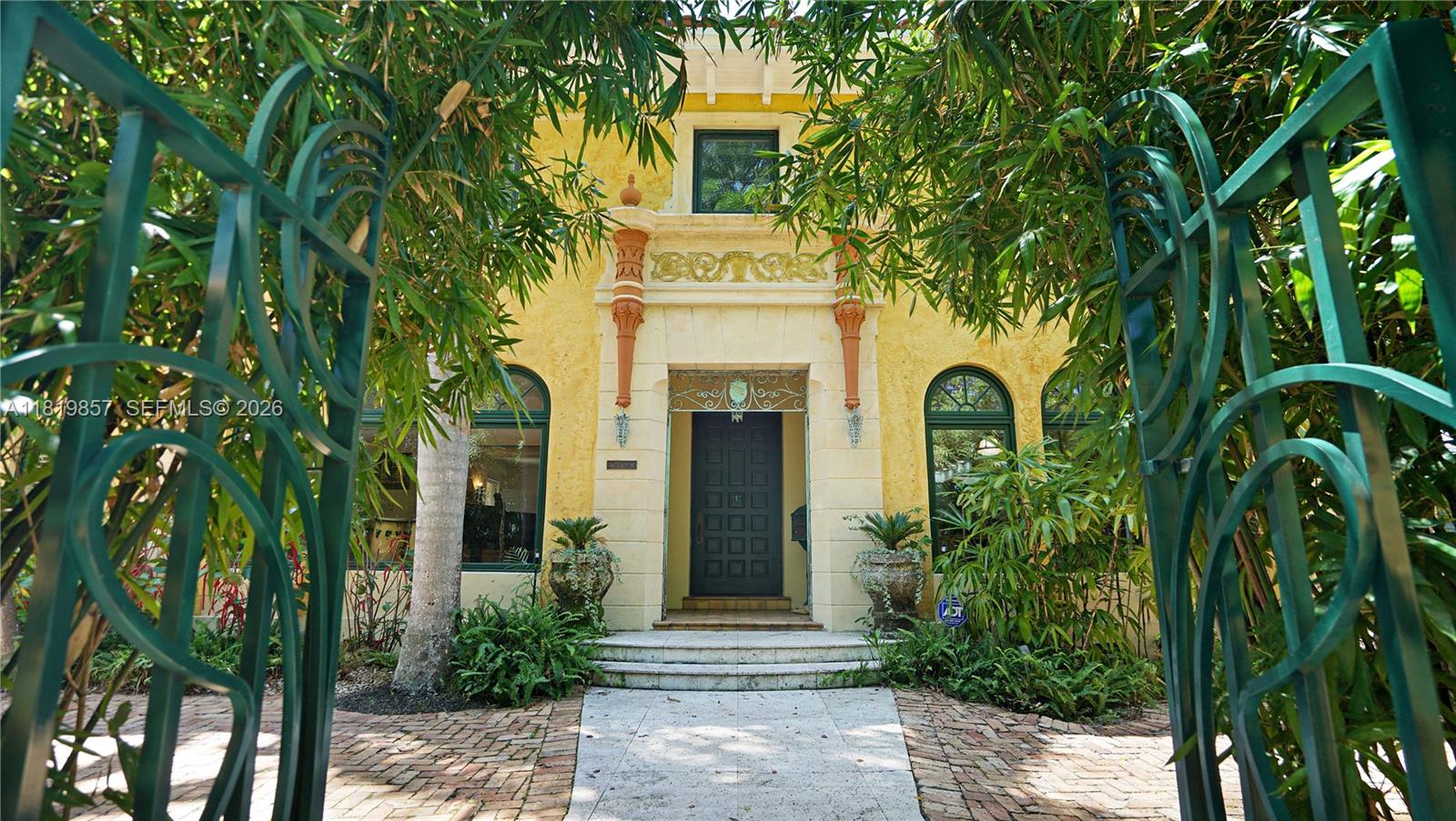 A yellow stucco house with a dark door is viewed through an ornate green gate — 2050 Alton Rd, Miami Beach FL 33140, MIAMI BEACH, FL