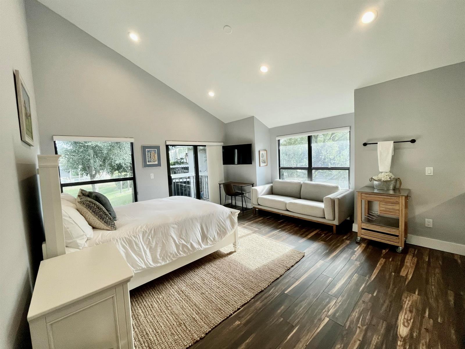 A bedroom features a vaulted ceiling, wood-look flooring, a bed, a sofa, and a desk — 11863 Wimbledon Circle # 547, Wellington FL 33414, WELLINGTON, FL