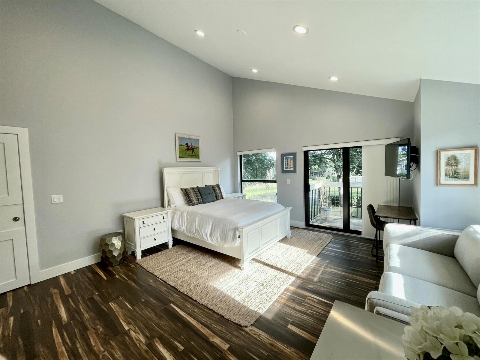 A bedroom features a white bed, dark wood-look flooring, a vaulted ceiling, and a sliding door — 11863 Wimbledon Circle # 547, Wellington FL 33414, WELLINGTON, FL