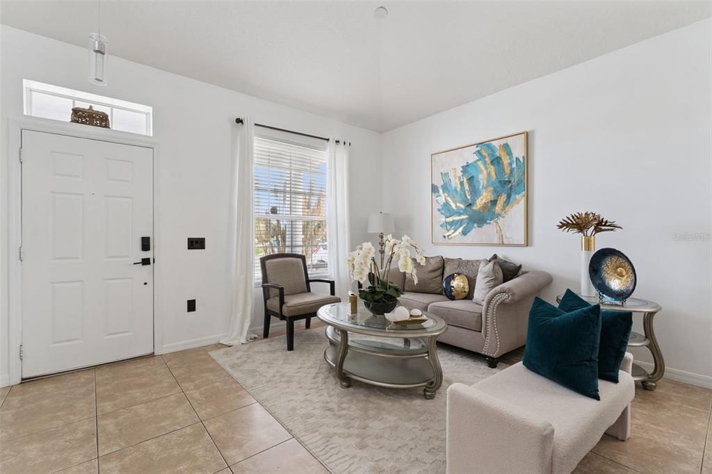 A bright living room features tile flooring, a beige sofa, an armchair, and wall art — 10484 EASTPARK LAKE DRIVE, ORLANDO, FL