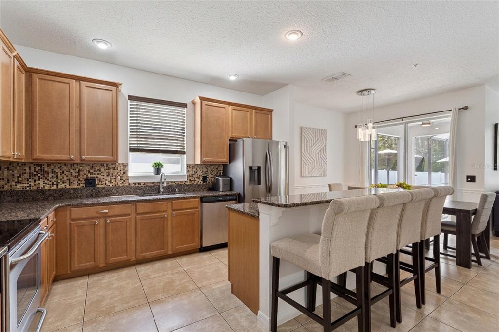 A kitchen features wood cabinets, granite countertops, a tile backsplash, and a breakfast bar — 10484 EASTPARK LAKE DRIVE, ORLANDO, FL