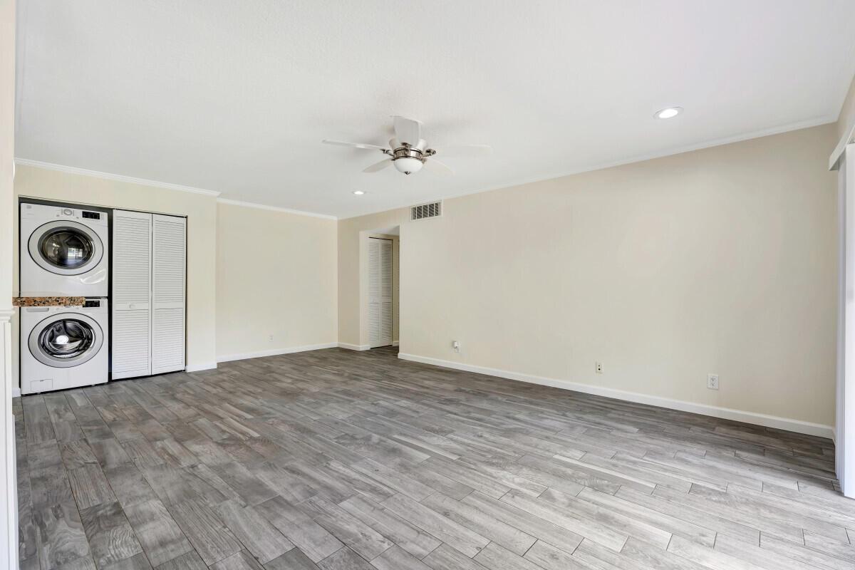 A room with light-colored walls, wood-look tile flooring, a ceiling fan, and stacked laundry appliances — 150 Pineview Road # F3, Jupiter FL 33469, JUPITER, FL