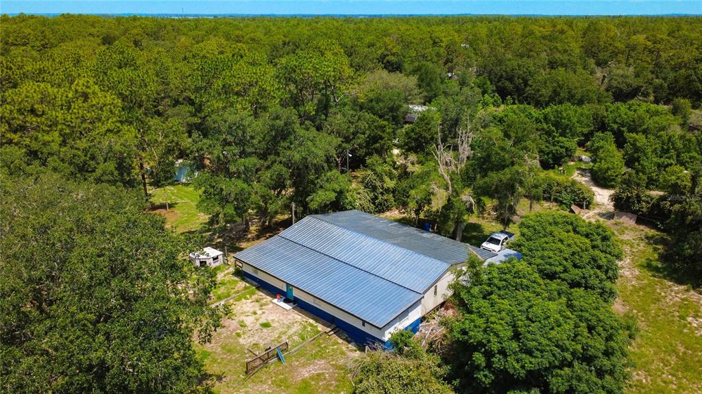 An aerial view shows a single-story house with a blue metal roof amidst wooded land — 13300 SW 91ST PLACE, DUNNELLON, FL