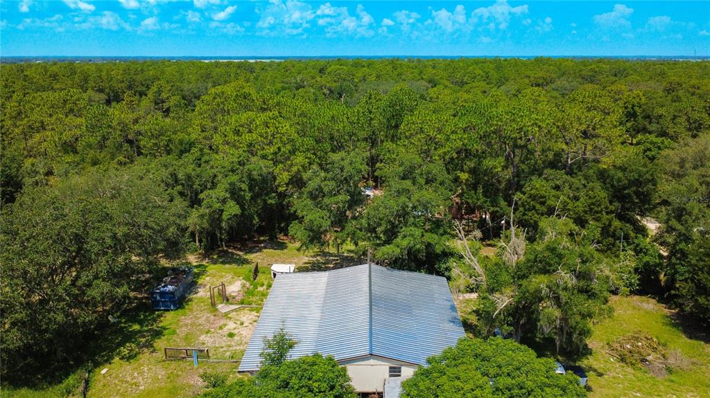 An aerial view shows a house with a metal roof surrounded by dense forest — 13300 SW 91ST PLACE, DUNNELLON, FL